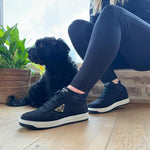 A woman in blue leggings and navy trainers sitting on a patio beside a small black dog, wearing black alpaca ankle socks.