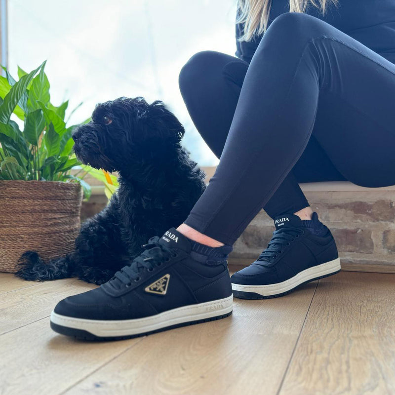 A woman in blue leggings and navy trainers sitting on a patio beside a small black dog, wearing black alpaca ankle socks.