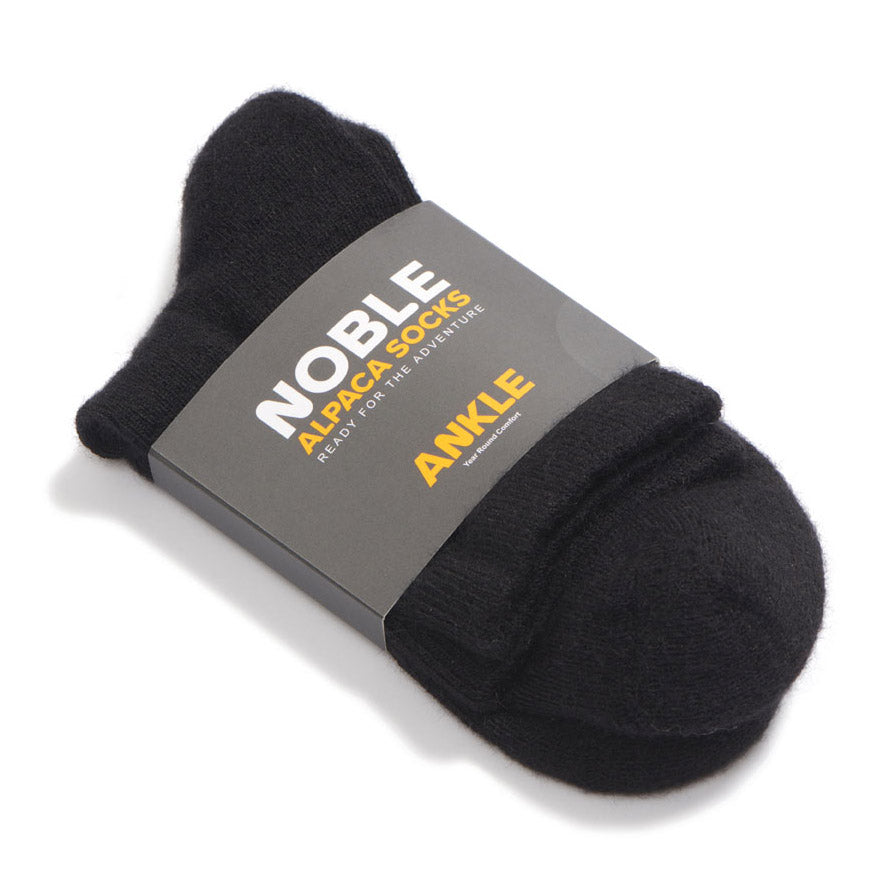 A black alpaca ankle sock in a Noble Alpaca Socks paper band, photographed on a white background.