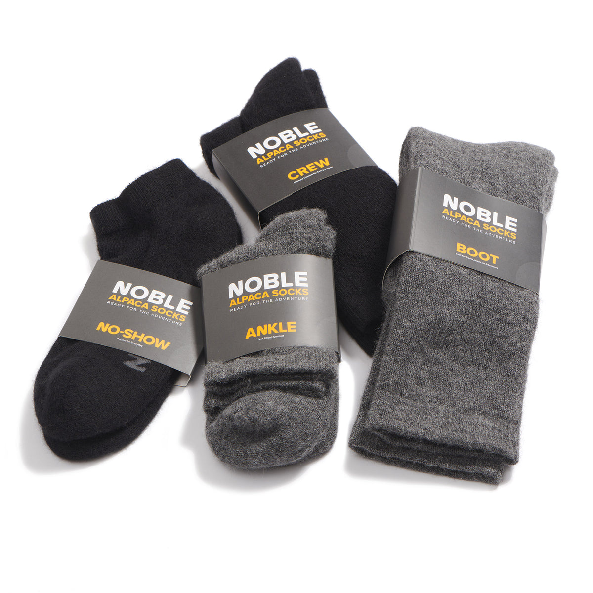 Four pairs of NOBLE brand knit socks in black and gray, including crew, ankle, boot, and no-show styles, arranged on a white background with dark paper bands around the cuffs.
