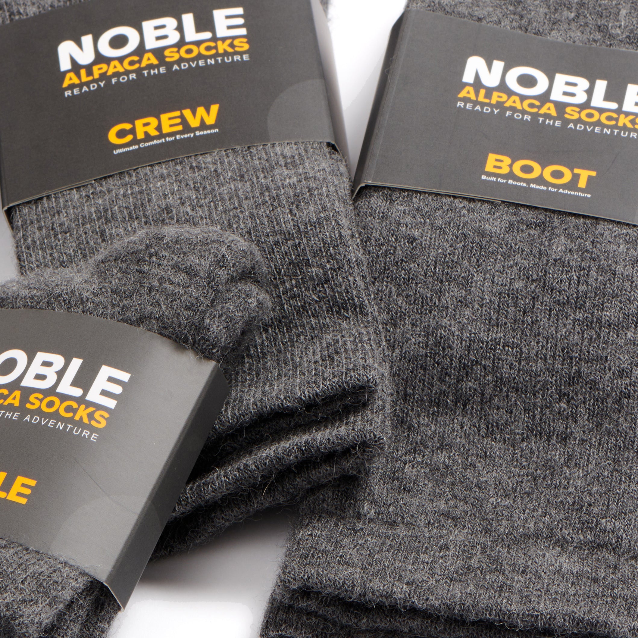 Three pairs of dark gray heathered alpaca socks with black paper bands displaying the 'NOBLE' brand logo, arranged on a white background.