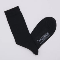 A pair of plain black merino wool crew socks laid flat on a pale grey background.
