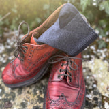A pair of grey marl merino socks tucked into red leather brogue shoes on a stone surface.