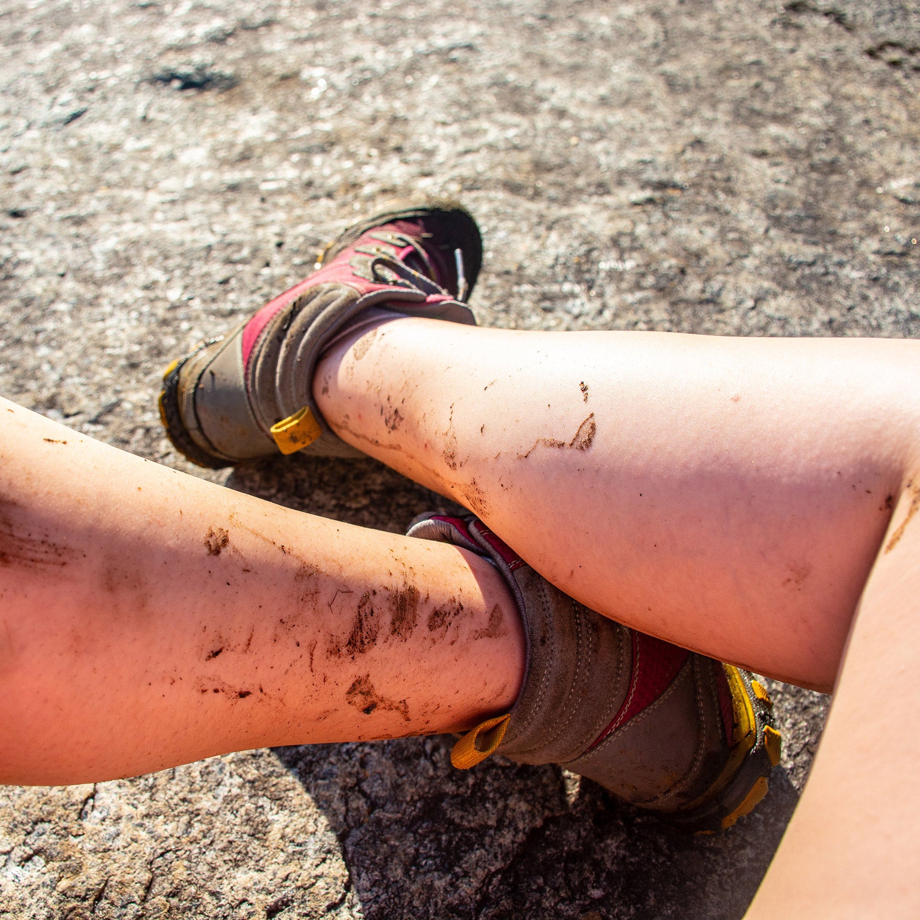 Mud-splashed bare legs in walking sandals resting on a rock, showing how alpaca no-show socks stay hidden.