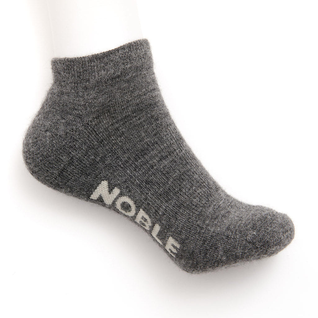 A grey marl alpaca no-show sock with the Noble logo knitted into the sole, shown on a white background.